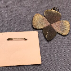 May include: A gold-toned metal pin in the shape of a four-leaf clover. The pin has a safety pin closure and is on a pink backing card.