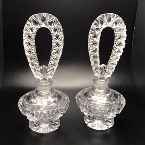 Puede incluir: Dos frascos de perfume de vidrio transparente con cortes en forma de diamante y asas de cristal ornamentadas. Los frascos tienen un aspecto vintage.