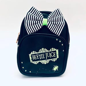 May include: Black faux leather backpack with a green and white striped bow, a green "Beetlejuice" logo, and a small green beetle graphic.