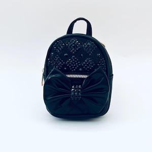 May include: A small black backpack with a large black bow on the front. The backpack is covered in black rhinestones.
