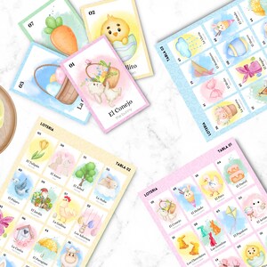 May include: A collection of colorful Loteria cards with Easter-themed illustrations, including bunnies, chicks, and eggs. The cards are arranged on a white marble surface, with some cards displaying the text "El Conejo" and "Loteria".