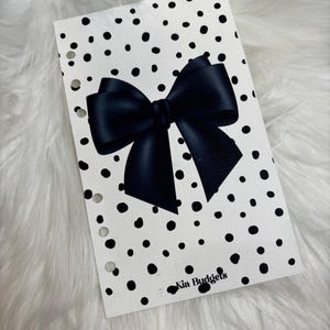 Op de afbeelding: Een witte plannerpagina met zwarte stippen en een grote zwarte strik in het midden. De tekst "Kia Budgets" staat onderaan de pagina.