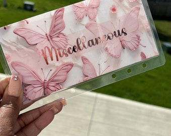 May include: A clear plastic sheet with a pink and white butterfly design. The sheet has the word "Miscellaneous" written in gold lettering. The sheet is designed for use in a planner or journal.