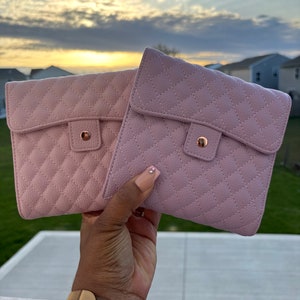 May include: Two quilted pink pouches with gold hardware and a flap closure. The pouches are held in a hand.