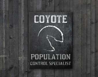 Könnte beinhalten: Ein schwarz-weißes Schild mit dem Text "Coyote Population Control Specialist" und einer Silhouette eines heulenden Kojoten. Das Schild hängt an einer schwarzen Holzwand mit einem Weidenkorb und einer Topfpflanze davor.