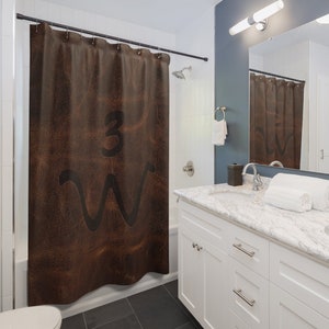 May include: Brown leather shower curtain with a black "3W" design. The shower curtain is hanging in a bathroom with white tile and a white vanity.