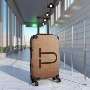 May include: A brown suitcase with a black handle and wheels. The suitcase has a brown leather-like texture and a black letter "P" on the front.