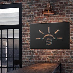 May include: A black metal sign with a stylised sun and the letter "S" in the centre. The sign is hanging on a brick wall with a copper light fixture above it.