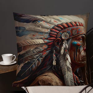 Pode incluir: Almofada decorativa com um retrato detalhado de um chefe nativo americano. A almofada apresenta um cocar vibrante com penas em tons de vermelho, azul e branco. O rosto do chefe é pintado com marcas tradicionais, criando um design marcante e artístico.