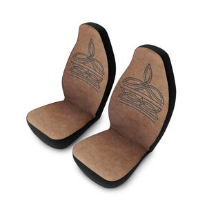 May include: Two car seat covers with a brown suede-like texture and black trim. Each cover features an embroidered design in a darker brown color. The covers are designed to fit standard car seats.