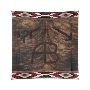 May include: A brown and black cowhide throw pillow with a red, white, and black geometric pattern border. The pillow features a brown leather brand with the letters "AB" in the center.