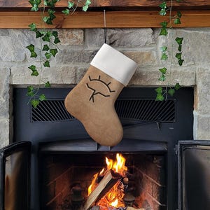 May include: A brown felt Christmas stocking with a white cuff and a black eye design hanging above a fireplace with a fire burning inside.