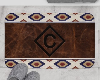 May include: Brown leather bath mat with a geometric pattern border in shades of blue, red, and white. The center of the mat features a large diamond shape with the letter "C" in black.
