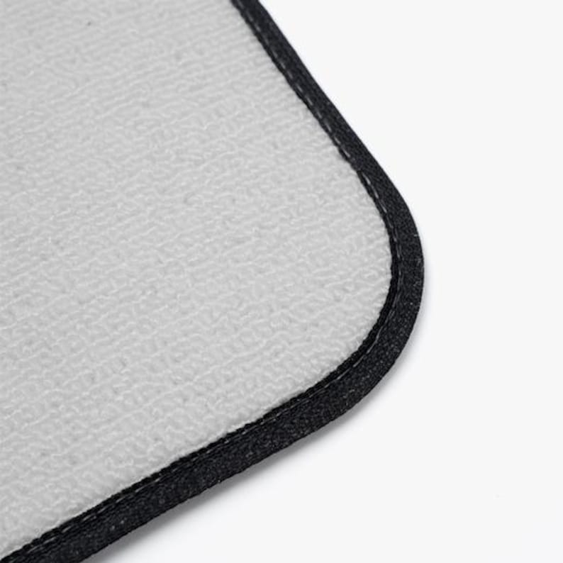 May include: A rectangular mouse pad with a light gray, textured fabric surface and a rounded corner. The edges of the mouse pad are finished with a thick, black stitched border that provides a clean and durable frame for the light gray center.