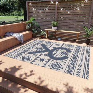 May include: An outdoor area rug with a geometric pattern in cream and navy blue. The rug features a large, stylized letter "XC" in the center. The design includes diamond, triangle, and sunburst motifs, creating a Southwestern or tribal aesthetic.