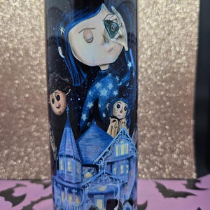 Pode incluir: Um copo alto e cil&iacute;ndrico com uma ilustra&ccedil;&atilde;o detalhada do filme de anima&ccedil;&atilde;o Coraline. O design inclui personagens, uma casa azul e um c&eacute;u estrelado. O copo &eacute; principalmente azul escuro com uma tampa roxa.