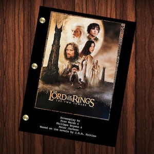 May include: A black script binder featuring the movie poster for "The Lord of the Rings: The Two Towers." The poster shows characters and a dark tower. The script binder has gold-colored fasteners and text at the bottom.