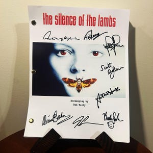 May include: A white script for the movie "The Silence of the Lambs" with a black and white photo of the main character with a moth over her mouth. The script is signed by the actors and director.