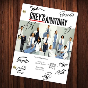May include: A black and white photo of the cast of Grey's Anatomy, a medical drama television series. The cast members are standing in a group, and the photo is signed by the cast members. The title of the episode is "A Hard Day's Night" and the writer is Shonda Rhimes and the director is Peter Horton.
