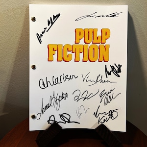 May include: A white script with the title "PULP FICTION" in yellow and red letters. The script is signed by several actors including Samuel L. Jackson, Uma Thurman, John Travolta, and Bruce Willis.