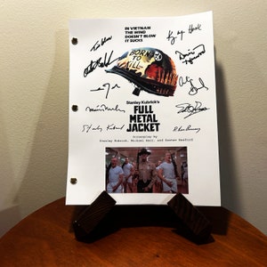 Può includere: Uno script bianco con testo nero che recita "Stanley Kubrick's Full Metal Jacket" con una foto in bianco e nero di un gruppo di uomini in uniforme militare. Lo script è firmato da diverse persone, tra cui Stanley Kubrick.
