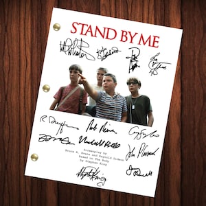May include: A black and white photo of four boys standing in a forest. The photo is a signed script from the movie "Stand By Me" with the title in red letters. The script is signed by the actors Wil Wheaton, River Phoenix, Corey Feldman, Jerry O'Connell, and the director Rob Reiner.
