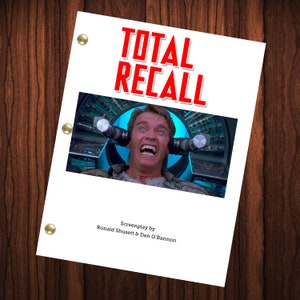 May include: A white script cover with the title "TOTAL RECALL" in red text. The cover features a photo of an actor with a shocked expression, wearing a blue shirt and sitting in a futuristic chair. The text "Screenplay by Ronald Shusett & Dan O'Bannon" is at the bottom of the cover.
