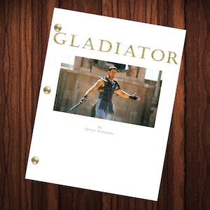 May include: A white script cover for the movie Gladiator, featuring a photo of Russell Crowe as Maximus Decimus Meridius in the arena. The title "GLADIATOR" is in gold lettering and the text "by David Franzoni" is at the bottom of the cover.