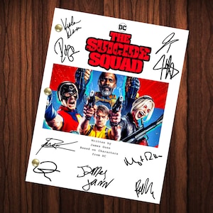 May include: A white script page with the title "The Suicide Squad" in bold red letters. The page features a photo of the main characters from the film, including Idris Elba, Margot Robbie, and John Cena. The page is signed by the cast and crew, including James Gunn, Margot Robbie, and John Cena.