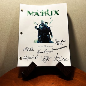 May include: A white script for "The Matrix" movie with signatures from the cast and crew, including Carrie-Anne Moss, Larry and Andy Wachowski, and Hugo Weaving. The script features a photo of the main characters from the movie.