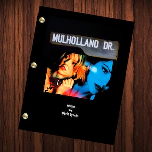 Peut inclure: Couverture de scénario noire avec une pancarte blanche qui indique "Mulholland Dr.". Deux femmes sont représentées sur la couverture, l'une avec des cheveux blonds et l'autre avec des cheveux foncés. Le texte "Écrit par David Lynch" est en bas de la couverture.