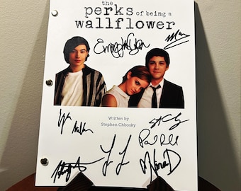 May include: A white script of "The Perks of Being a Wallflower" with images of the actors and their signatures. The script is held up by a brown stand. The text "Written by Stephen Chbosky" is also visible.