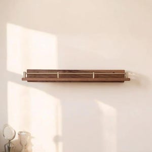 May include: A wooden wall shelf with brass accents. The shelf is mounted on a white wall and has a light wood finish.