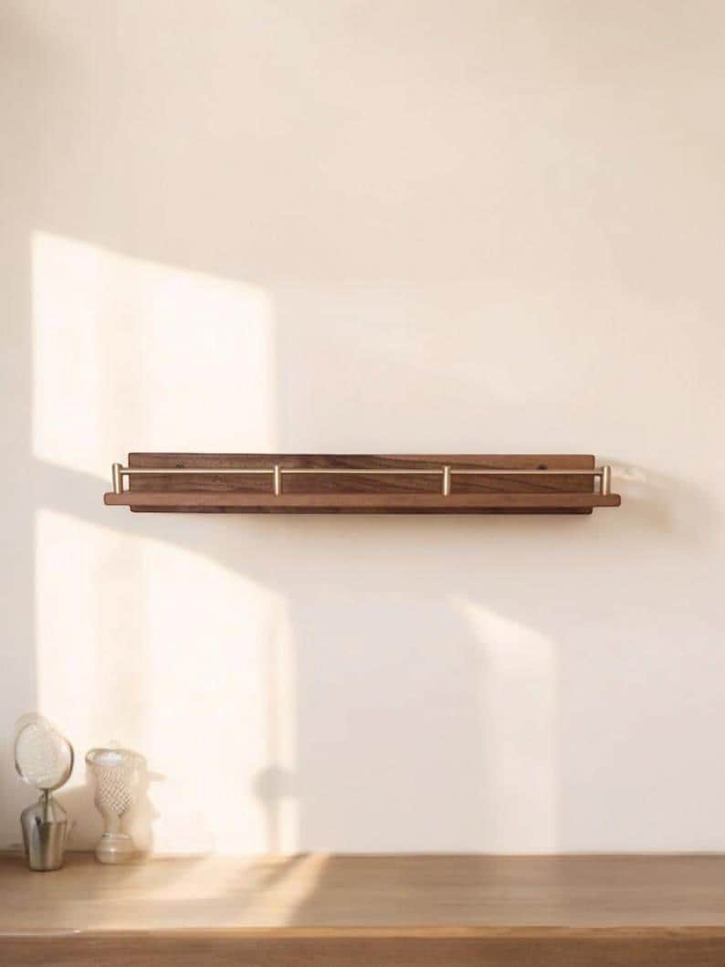 May include: A wooden wall shelf with brass accents. The shelf is mounted on a white wall and has a light wood finish.