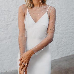 May include: A white sheer top with long sleeves and pearl embellishments. The top is made of a delicate fabric and has a loose, flowing fit.