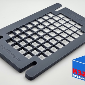 Può includere: Griglia rettangolare grigia con aperture quadrate. Il prodotto ha estensioni a forma di maniglia ad ogni estremità. I testi "2 Degrees" e "K32 Designs" sono visibili. Un logo blu e rosso si trova in basso a destra.