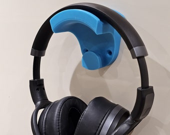 Op de afbeelding: Een blauwe 3D-geprinte koptelefoonhouder gemonteerd op een witte muur met een zwarte koptelefoon die eraan hangt.