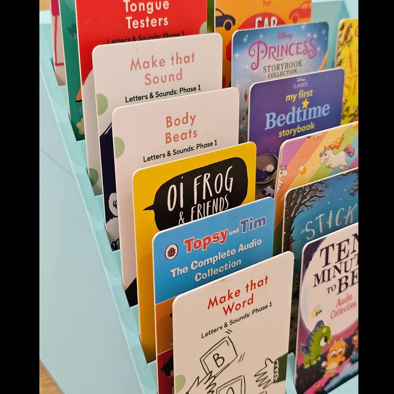 Puede incluir: Una colecci&oacute;n de libros y colecciones de audio para ni&ntilde;os en un organizador azul claro. Los libros tienen portadas coloridas con t&iacute;tulos como "Princess Storybook Collection", "Oi Frog & Friends" y "Ten Minutes to Bed".