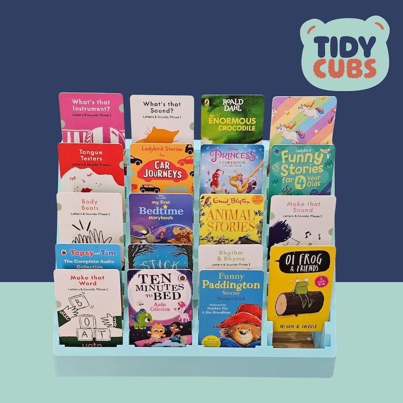 Puede incluir: Una estanter&iacute;a azul claro llena de coloridos libros infantiles. Los t&iacute;tulos incluyen "Enormous Crocodile", "Princess Storybook" y "Funny Paddington". El logotipo de "Tidy Cubs" es visible en la esquina superior derecha.