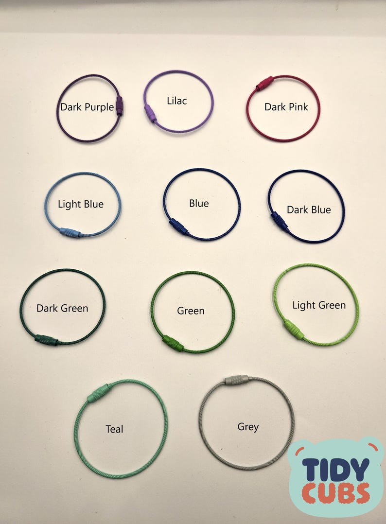 May include: Assortment of ten colorful key rings in various colors including lilac, dark purple, dark pink, light blue, blue, dark blue, dark green, green, light green, teal, and grey. The key rings are made of metal and have a small metal loop at the top.