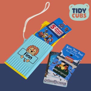 May include: A light blue book holder with a yellow trim, featuring a lion illustration and the name "Finn." It contains several children's books, including a "5-Minute Stories Collection" and "Row Your Boat." The "Tidy Cubs" logo is visible.
