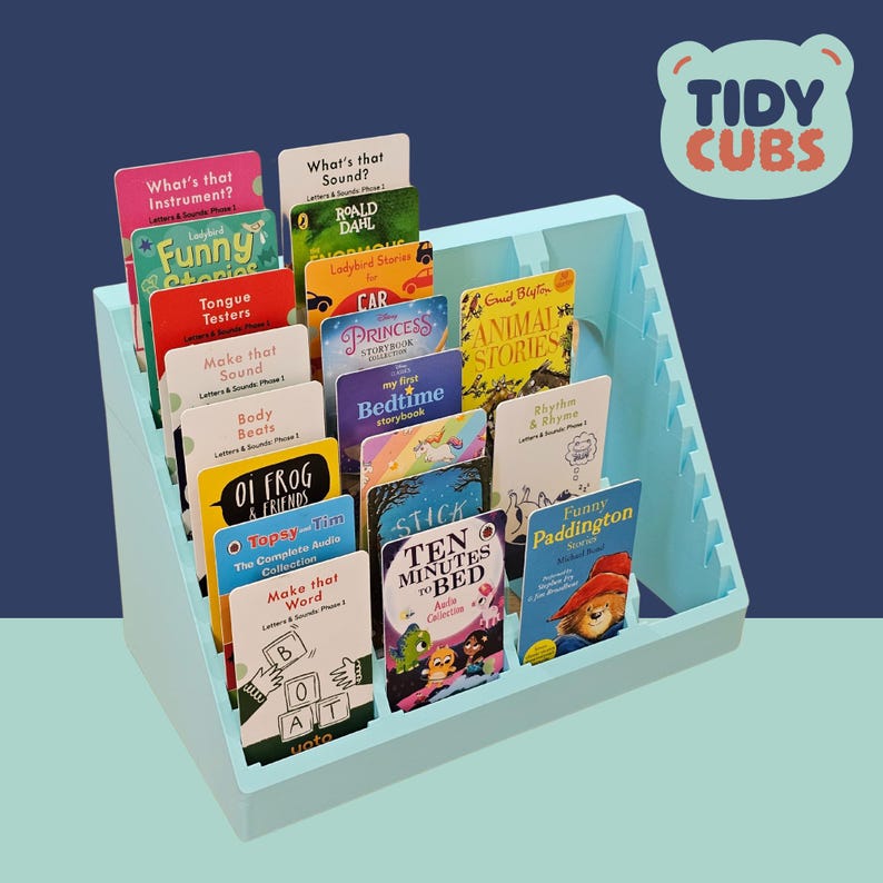 Puede incluir: Un organizador de libros azul claro lleno de libros infantiles coloridos. Los t&iacute;tulos incluyen "Funny Stories", "Princess Storybook" y "Ten Minutes to Bed". El organizador tiene el texto "Tidy Cubs".
