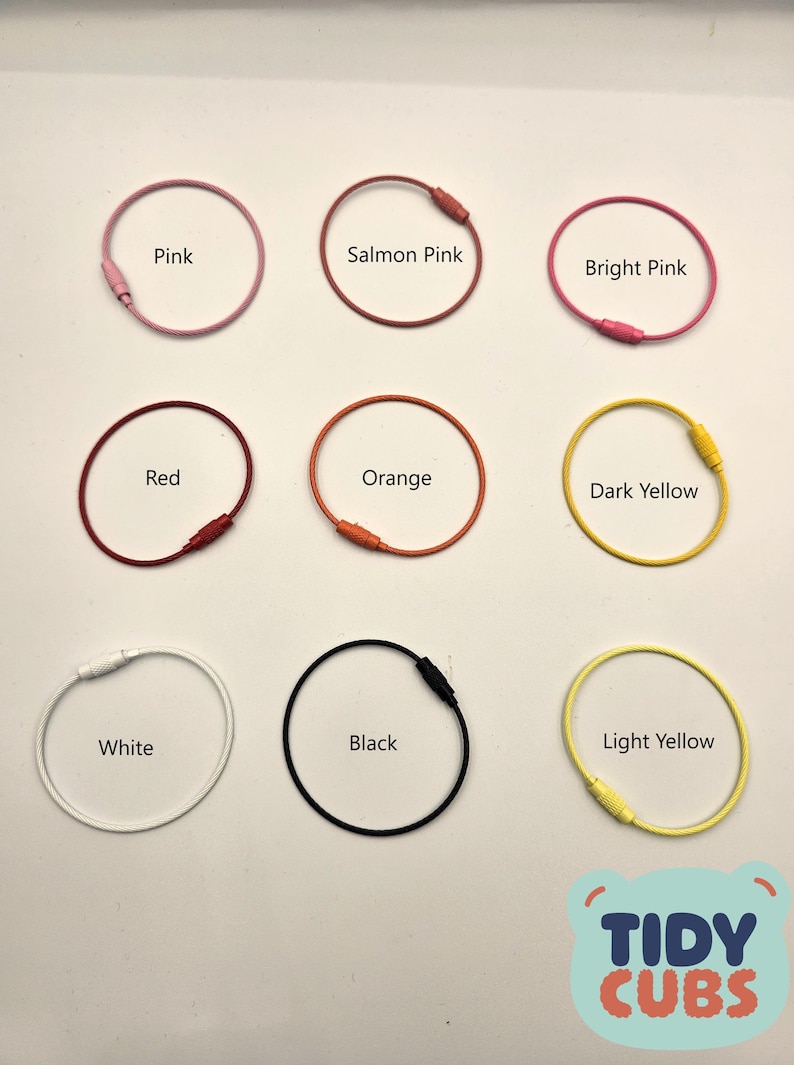 May include: Nine colorful metal key rings in various colors including pink, red, orange, yellow, white, and black. The key rings are arranged in three rows of three. The text "TIDY CUBS" is visible in the bottom right corner of the image.