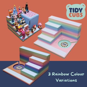 Może przedstawiać: Trzy trójstopniowe stojaki wystawowe w kolorach tęczy, każdy z okrągłym wycięciem w dolnym poziomie. Każdy stojak zawiera napis "TIDY CUBS" w białym kółku. Stojaki są przeznaczone do przechowywania małych zabawek lub figurek.
