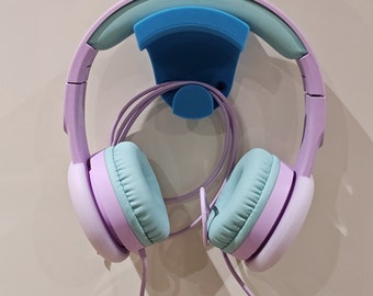 May include: A light blue and purple headphone holder with a light blue headphone hook. The headphone hook is attached to a white wall. The headphones are light purple with light blue earcups.