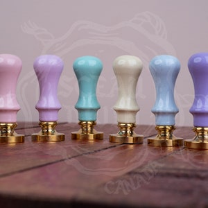 May include: Six pastel-coloured wax seal stamps with gold bases. The colours are pink, lavender, light blue, cream, blue, and purple.