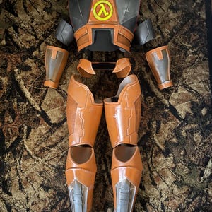 May include: An orange and gray cosplay costume, featuring a chest piece with a yellow lambda symbol, shoulder pads, arm guards, and leg armor. The costume is designed with a segmented, armored appearance.