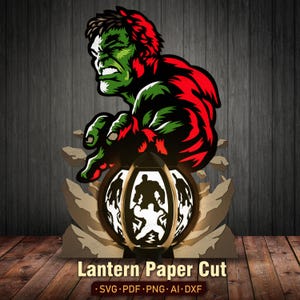 May include: A multi-layered paper cut design featuring a green and red muscular character above a spherical lantern. The lantern displays silhouettes of the same character. The text "Lantern Paper Cut" and "SVG PDF PNG AI DXF" is visible.