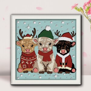 May include: A framed print featuring three Highland cows dressed for the holidays. One cow wears a reindeer antler hat and a red sweater. Another wears a green hat and red scarf. The third cow is in a Santa suit.