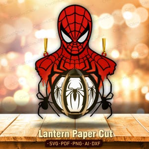 Può includere: Un design decorativo in carta ritagliata raffigurante il personaggio di Spider-Man in rosso e nero sopra una lanterna circolare. La lanterna mostra un emblema di ragno bianco su sfondo nero, affiancato da due sagome di ragni neri.